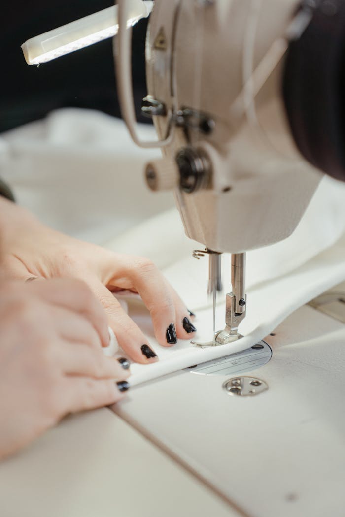 creative-01 Detailed view of a sewing machine stitching fabric with visible hands, nails painted black.