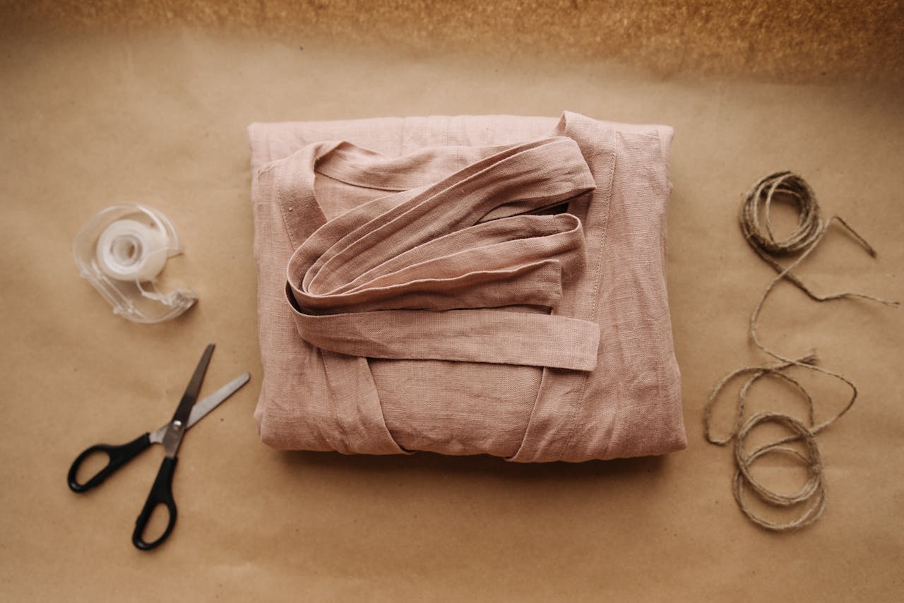 brand-01 Folded pink fabric with scissors, twine, and tape on brown paper, perfect for crafting themes.